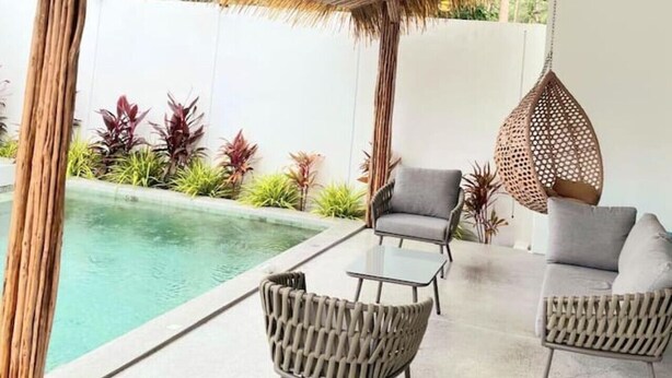 A poolside area with a thatched roof, wicker furniture, and hanging lights.
