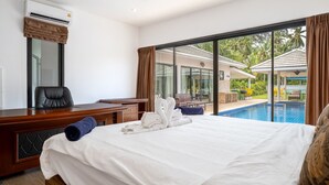 Une chambre d’hôtel avec un grand lit, un bureau avec une chaise, une fenêtre avec des rideaux et une vue sur une piscine et des palmiers.