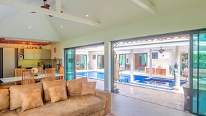 Un salon moderne avec un canapé et un coin repas, une cuisine, et une piscine visible à travers des portes vitrées.