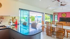 Une cuisine moderne dotée d’un îlot central en verre, d’un coin repas avec des chaises en bois et d’un ventilateur de plafond.