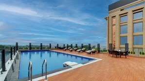A rooftop pool with lounge chairs and a table, surrounded by a wooden deck and a building with large windows. - Rajawat The Fern An Ecotel Hotel (Akbarpur)