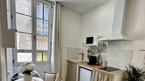 A compact kitchen with a dining area, featuring a small island, white cabinetry, and a microwave. - ✨ Cosy nest in the heart of Pézenas - Comfort & charm by Sandro (Pézenas)