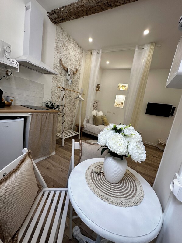 A compact living space with a kitchenette, a dining area with a white table and chairs, a sofa, and a TV mounted on the wall.
