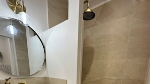 A bathroom with a white sink, gold faucet, and a round mirror. There are wicker baskets under the sink and a shower with beige tiles. - ✨ Cosy nest in the heart of Pézenas - Comfort & charm by Sandro (Pézenas)