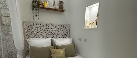A bedroom with a large bed, a decorative headboard, a small stool, and a shelf with decorative items.