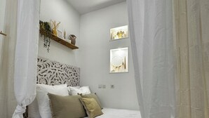 A bedroom with a bed, white curtains, a headboard, a small wooden stool, and wall-mounted decorations. - ✨ Cosy nest in the heart of Pézenas - Comfort & charm by Sandro (Pézenas)