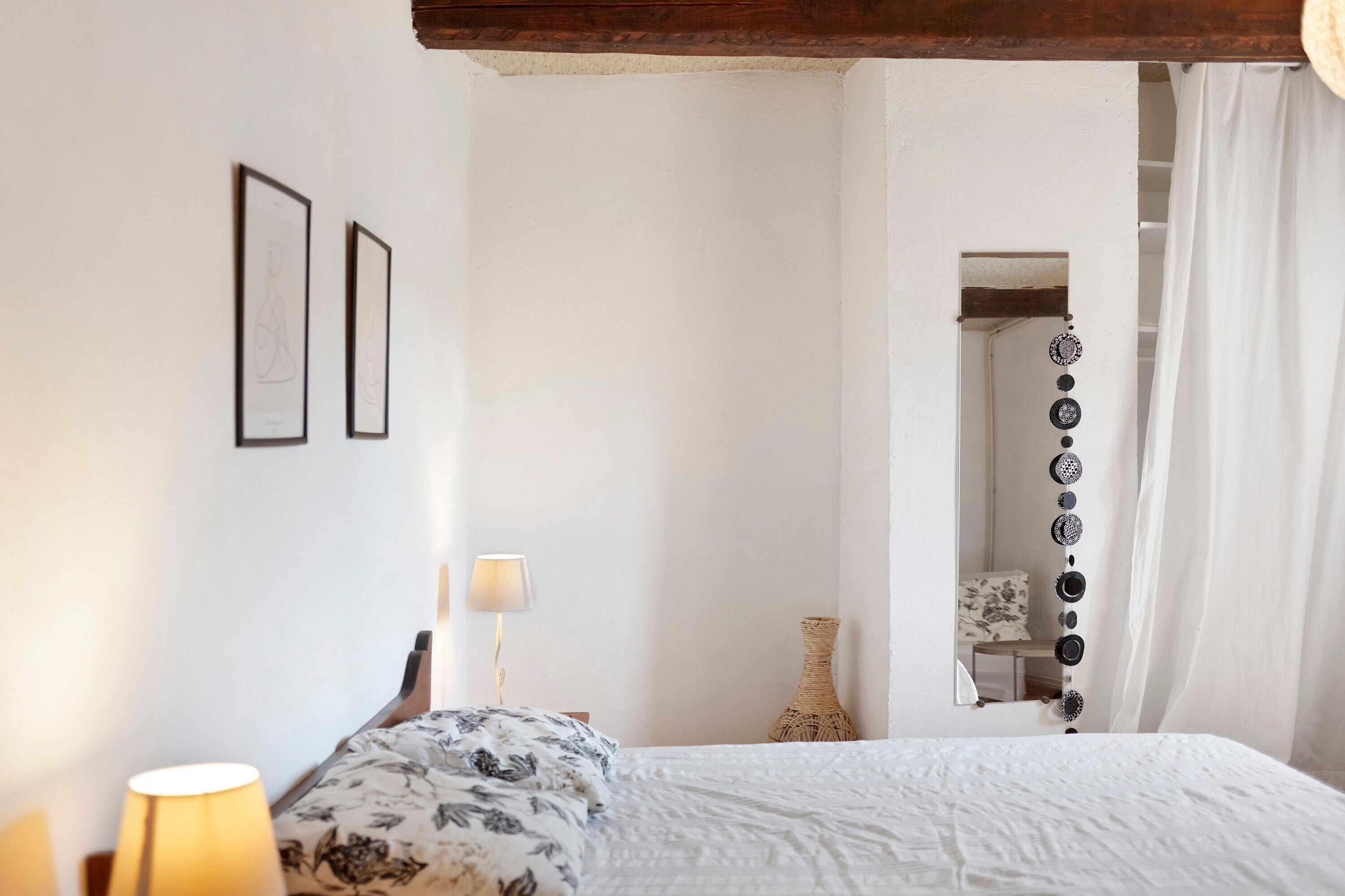 Ein Schlafzimmer mit einem Bett, einem Nachttisch, einer Lampe, gerahmten Bildern an der Wand und einem Spiegel.