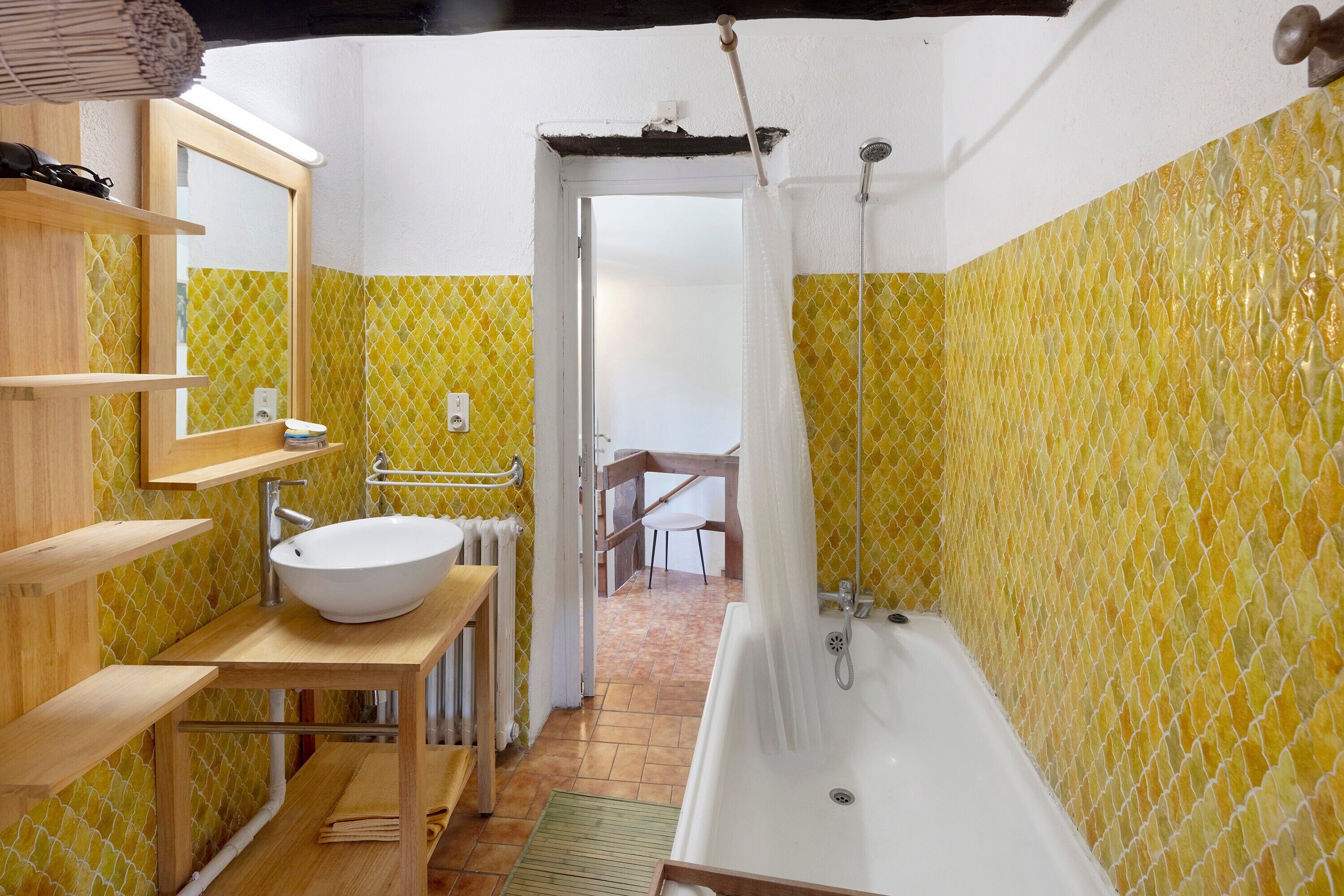 Ein Badezimmer mit einer Badewanne, einem Waschbecken und einem Spiegel. Ein Holzregal und ein Handtuchhalter sind ebenfalls vorhanden.