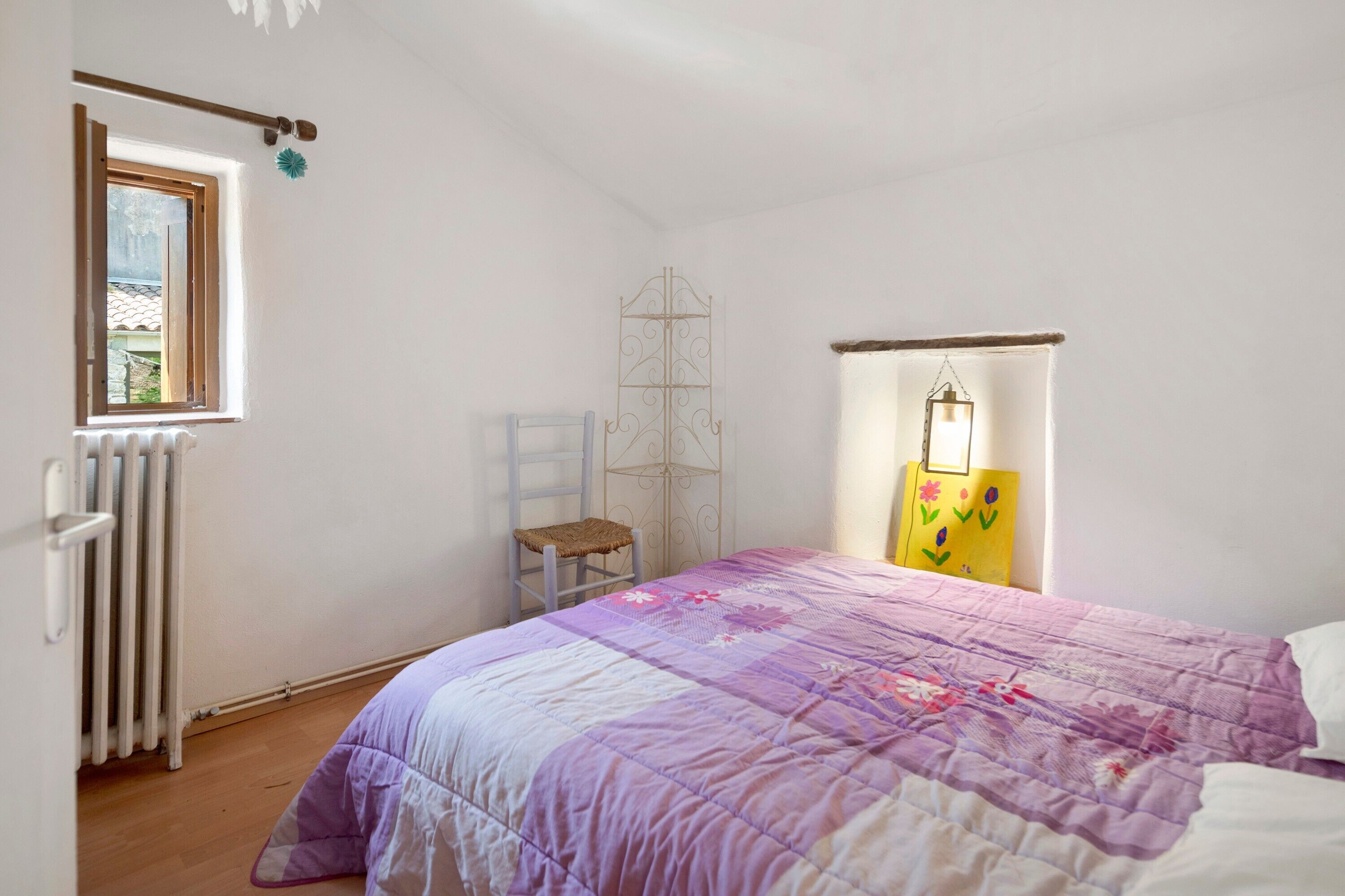 Une chambre à coucher avec un lit, une fenêtre, un radiateur, une chaise et une étagère.
