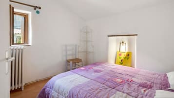 Une chambre à coucher avec un lit, une fenêtre, un radiateur, une chaise et une étagère.