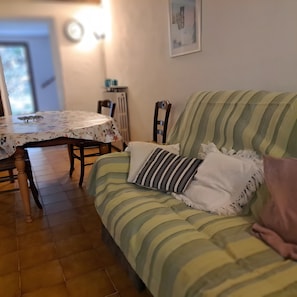 Una stanza accogliente con un divano a righe, un tavolo da pranzo con una tovaglia floreale e un termosifone.