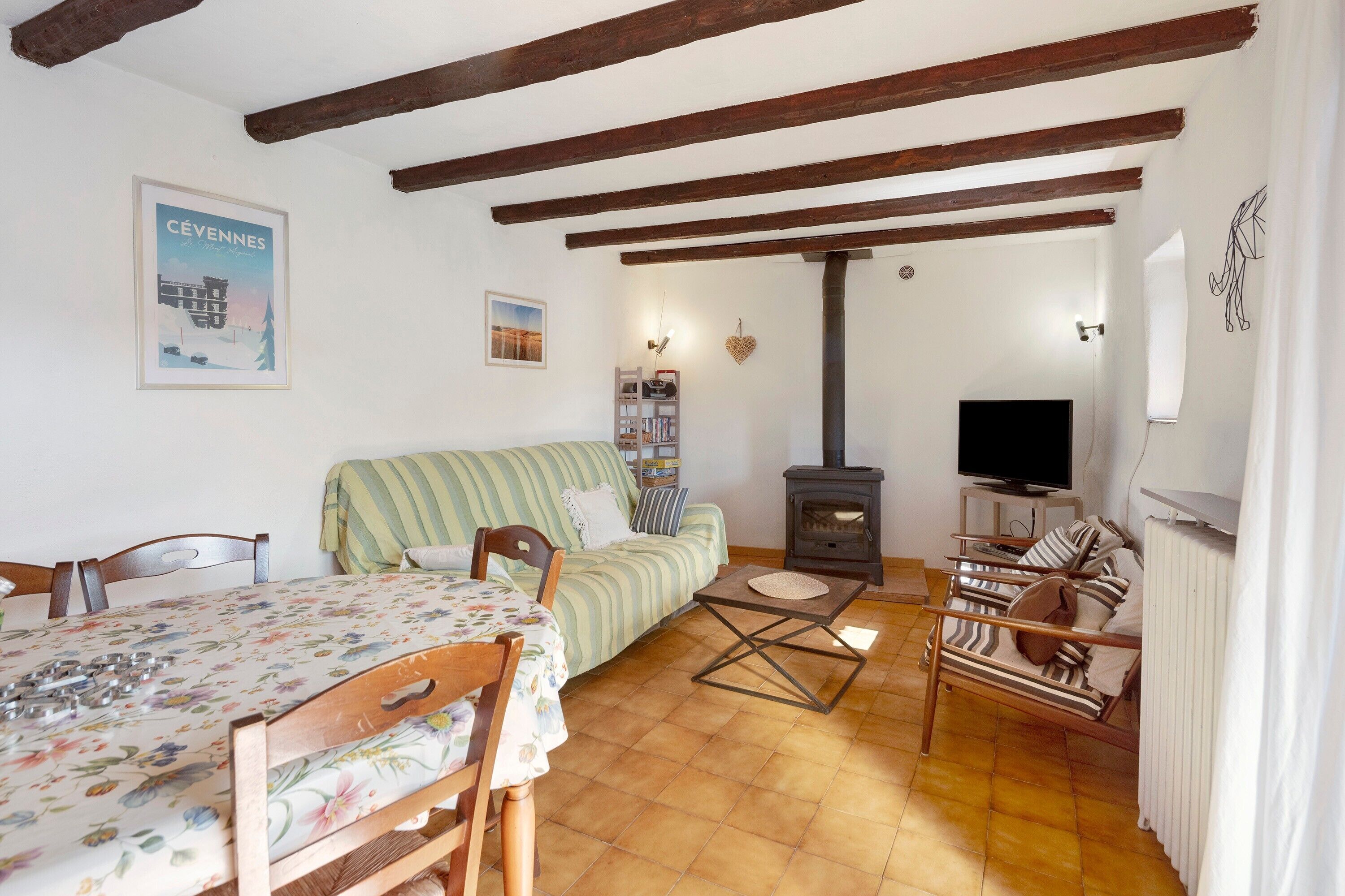Une pièce confortable avec un lit, un canapé, une table recouverte d’une nappe à motifs floraux, un téléviseur et un poêle à bois.