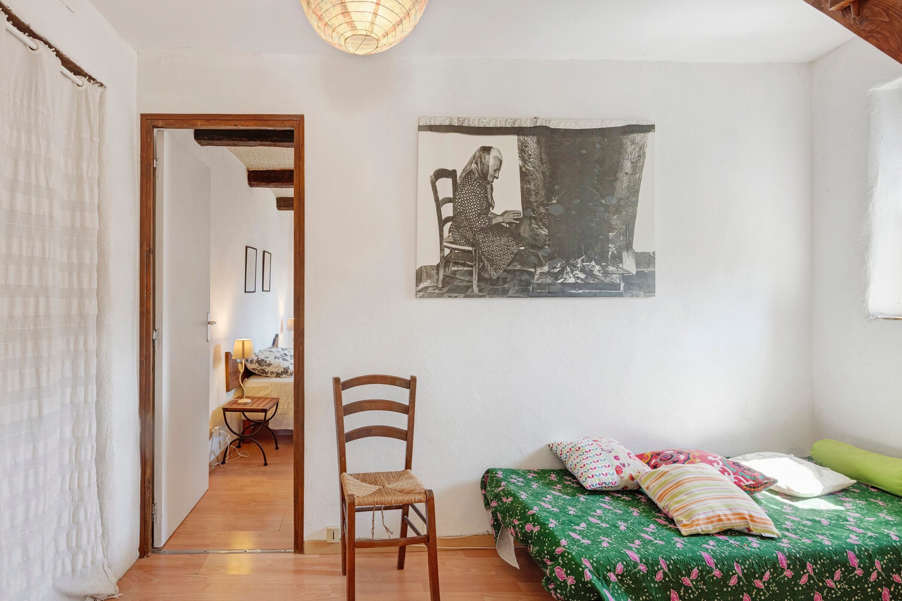Une chambre à coucher avec un lit, une chaise, un tableau et une porte donnant sur une autre pièce.