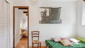 Une chambre à coucher avec un lit, une chaise, un tableau et une porte donnant sur une autre pièce.