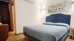 Une chambre à coucher avec un lit, une chaise, une lampe fixée au mur et un tableau.