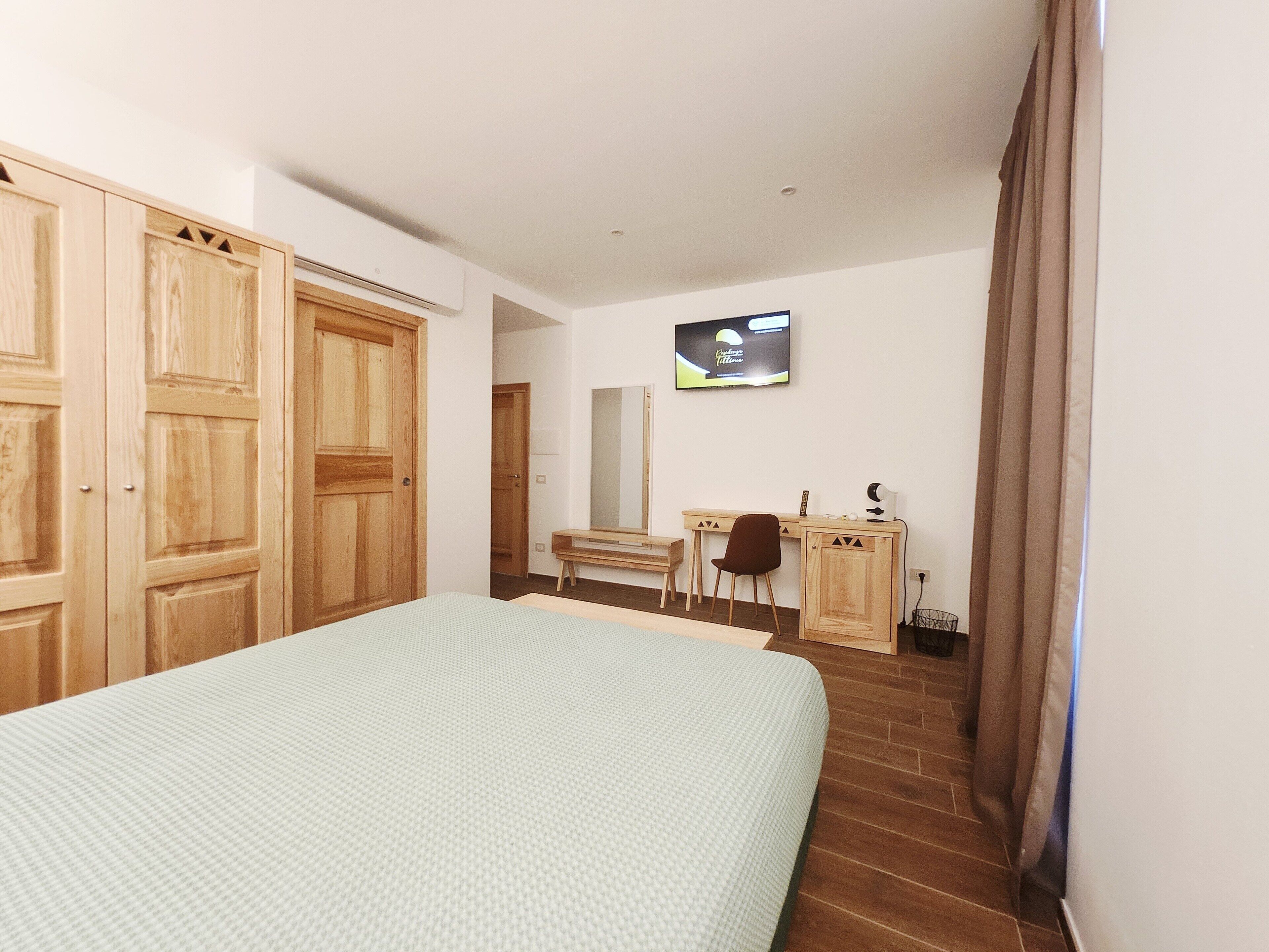 Een slaapkamer met een bed, bureau, stoel, kapstok en televisie aan de muur.