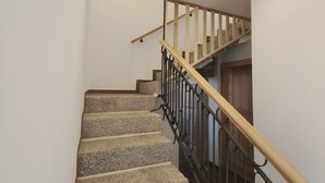 Un escalier avec des marches en pierre et une rampe en bois, menant à un palier doté d’une porte.