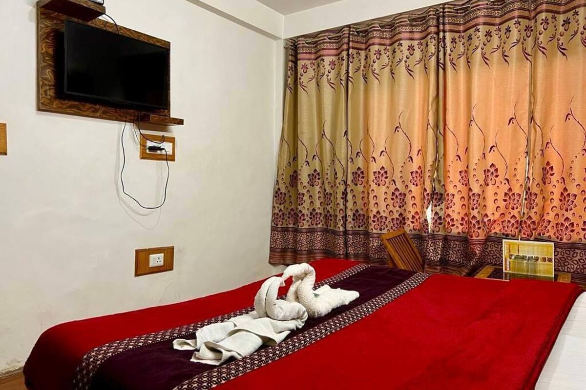 Habitación de hotel con cama, televisor de pantalla plana montado en la pared y cortina con estampado floral.