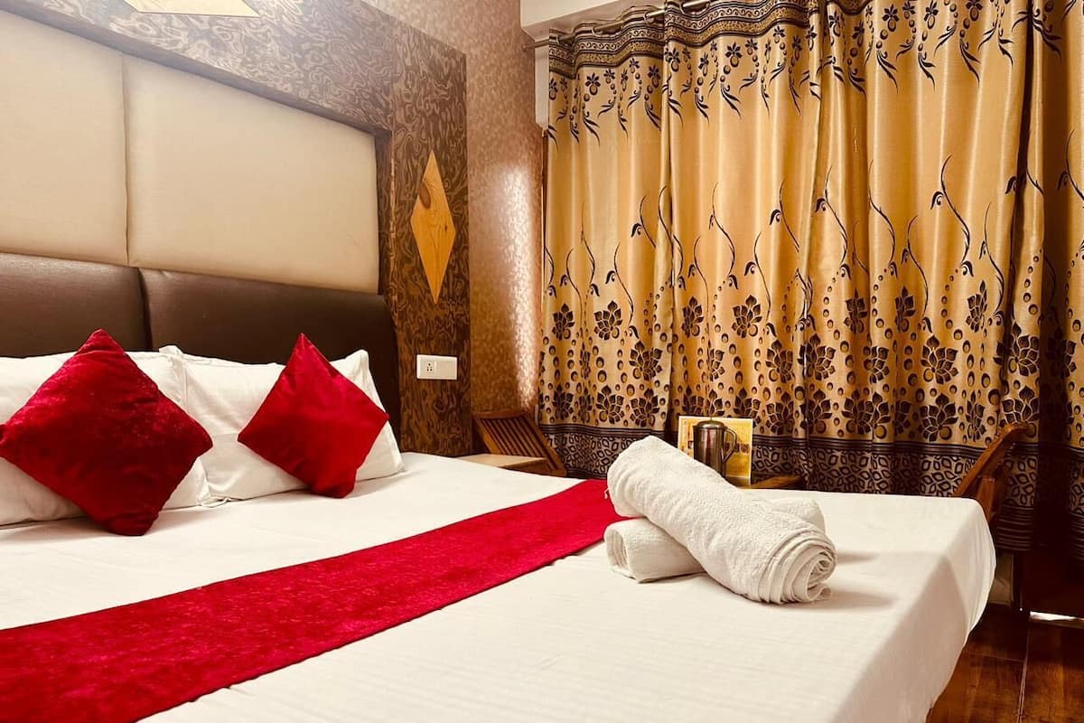 Habitación de hotel con una cama grande, almohadones rojos, una manta roja y una toalla blanca bien doblada.