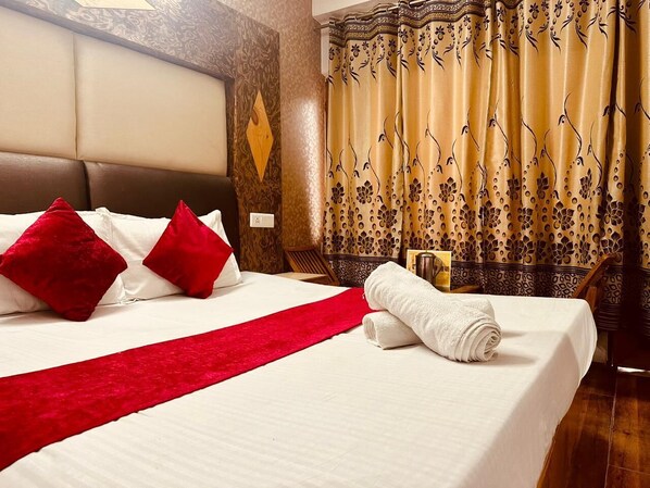 Une chambre d’hôtel avec un grand lit, des oreillers rouges, un plaid rouge et une serviette blanche soigneusement pliée.