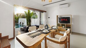 Un comedor moderno con una mesa de madera, sillas blancas y un amplio ventanal con vista a una piscina.