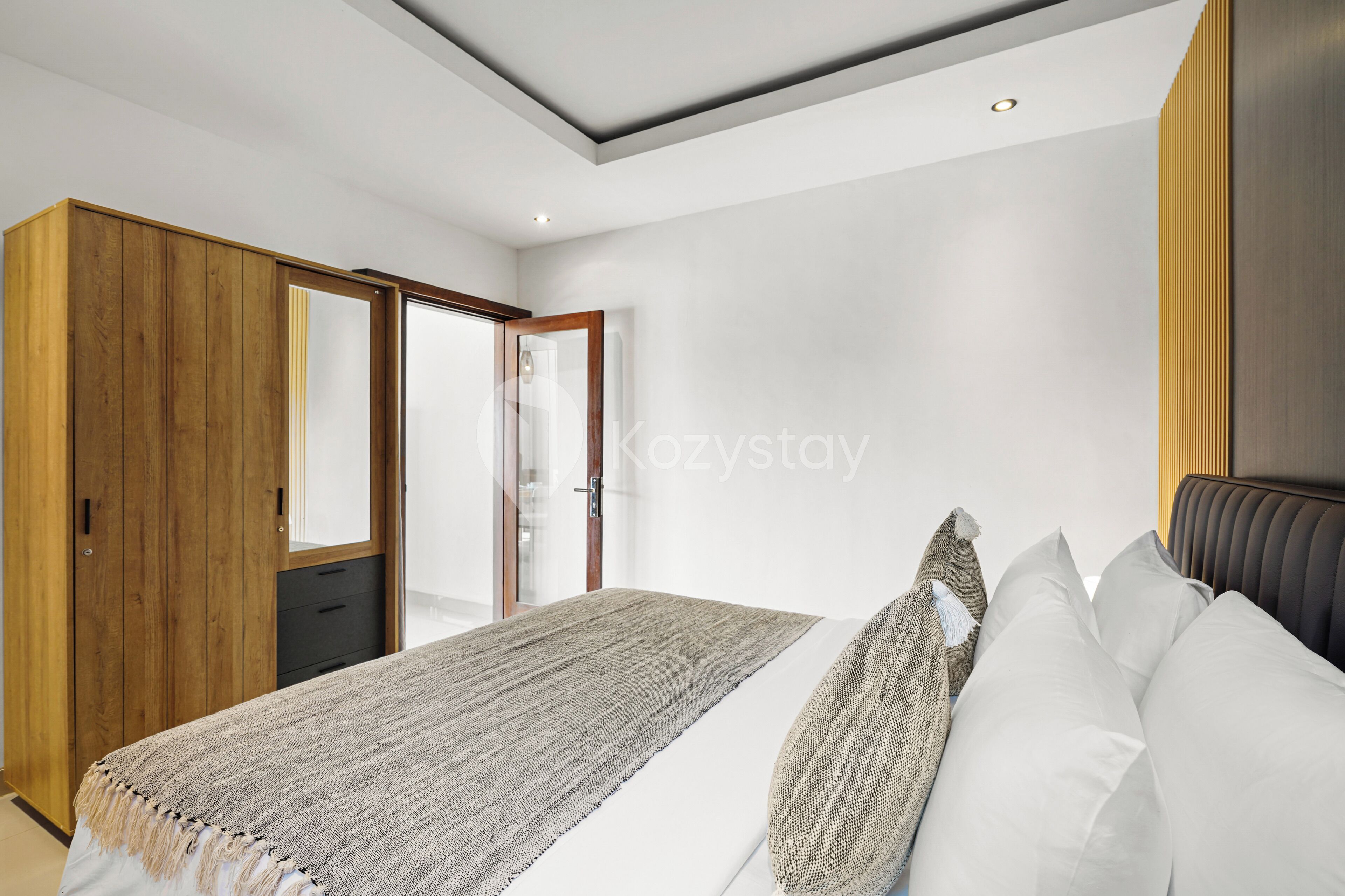 A modern bedroom with a large bed, a wooden wardrobe, and a sliding glass door leading to a balcony.