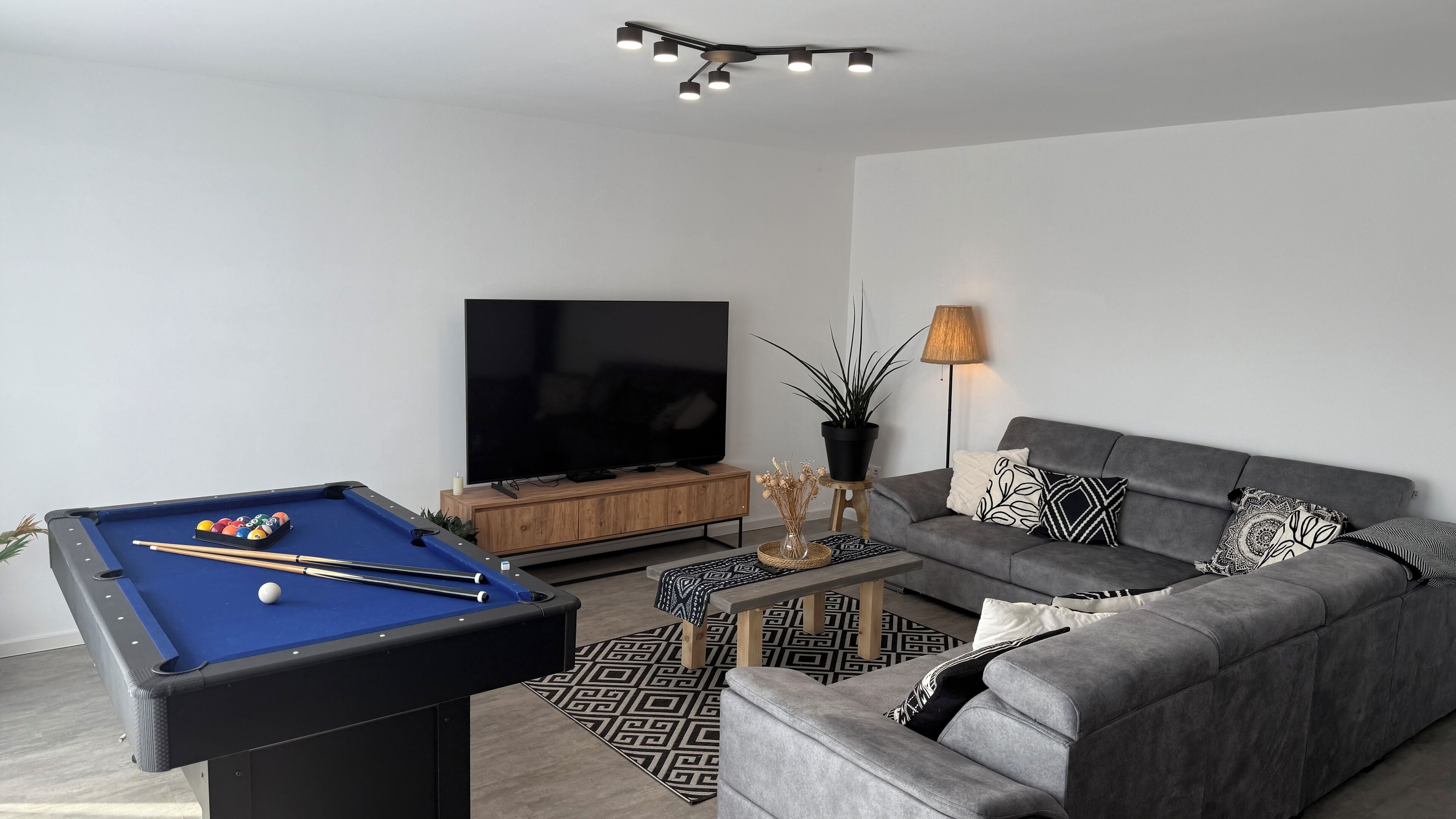 Un salon moderne avec une table de billard, un canapé, un téléviseur et une lampe.