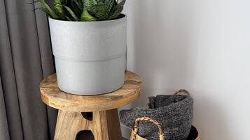 A grey potted plant with variegated leaves on a wooden stool next to a woven basket.