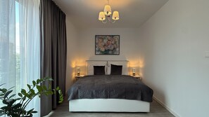 Ein modernes Schlafzimmer mit einem großen Bett, Nachttischlampen, einer Kandelaber und einem Blumenbild an der Wand.