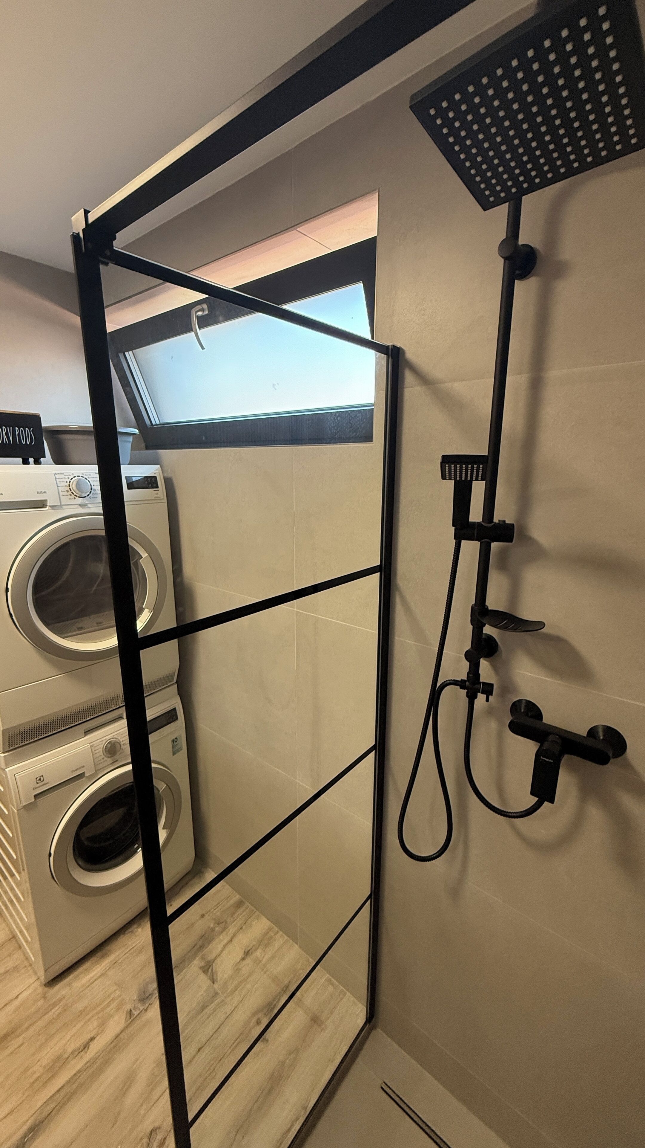 Une petite buanderie comprenant un lave-linge, un sèche-linge et un espace douche doté d’un panneau de commande.