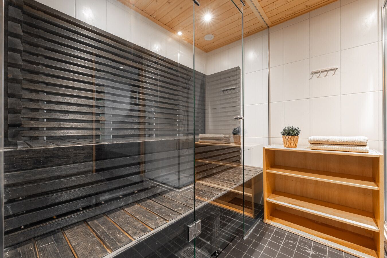 Ein modernes Badezimmer mit Duschabtrennung aus Glas, Holztritten, einem Holzwaschtisch und einer kleinen Pflanze.