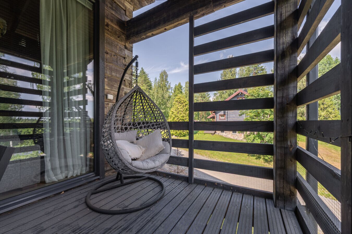 Eine Holzterrasse mit einer Hängematte und Blick auf ein Haus im Hintergrund.
