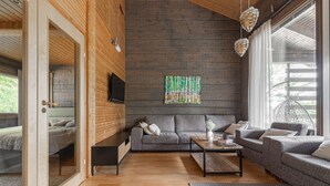 A modern living room with a wooden ceiling, a grey sofa set, a coffee table, and a large window with a view of greenery.