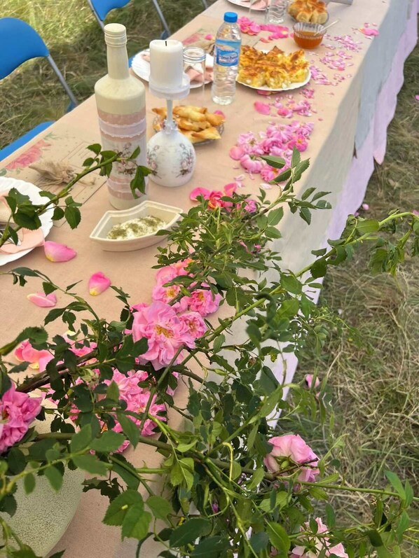 Une table dressée à l’extérieur, recouverte d’une nappe rose, agrémentée de décorations florales et présentant une variété de plats.