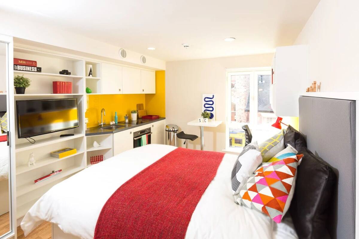 Habitación de hotel moderna con cama, televisión, kitchenette pequeña y vista a la ciudad.
