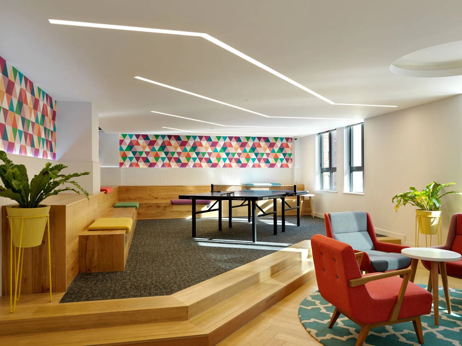 A modern office space with a long table, colorful geometric wall art, and a variety of seating options including a sofa and chairs.