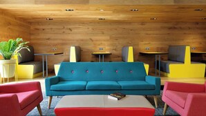 A modern lounge area with a teal sofa, red armchairs, and yellow and gray accent chairs. There are small tables and a potted plant. - For Students Only - Modern Rooms in York (York)