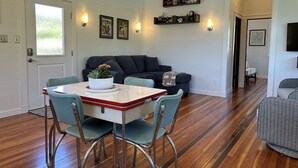 A dining area with a table and chairs, a sofa, and a television in the background. - Float House No. 2 at Jack Creek (Astoria)