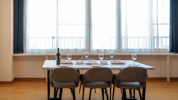 A dining area with a table set for four, large windows with curtains, and a view of the outside. - STAY IN TOKIWA (Asahikawa)