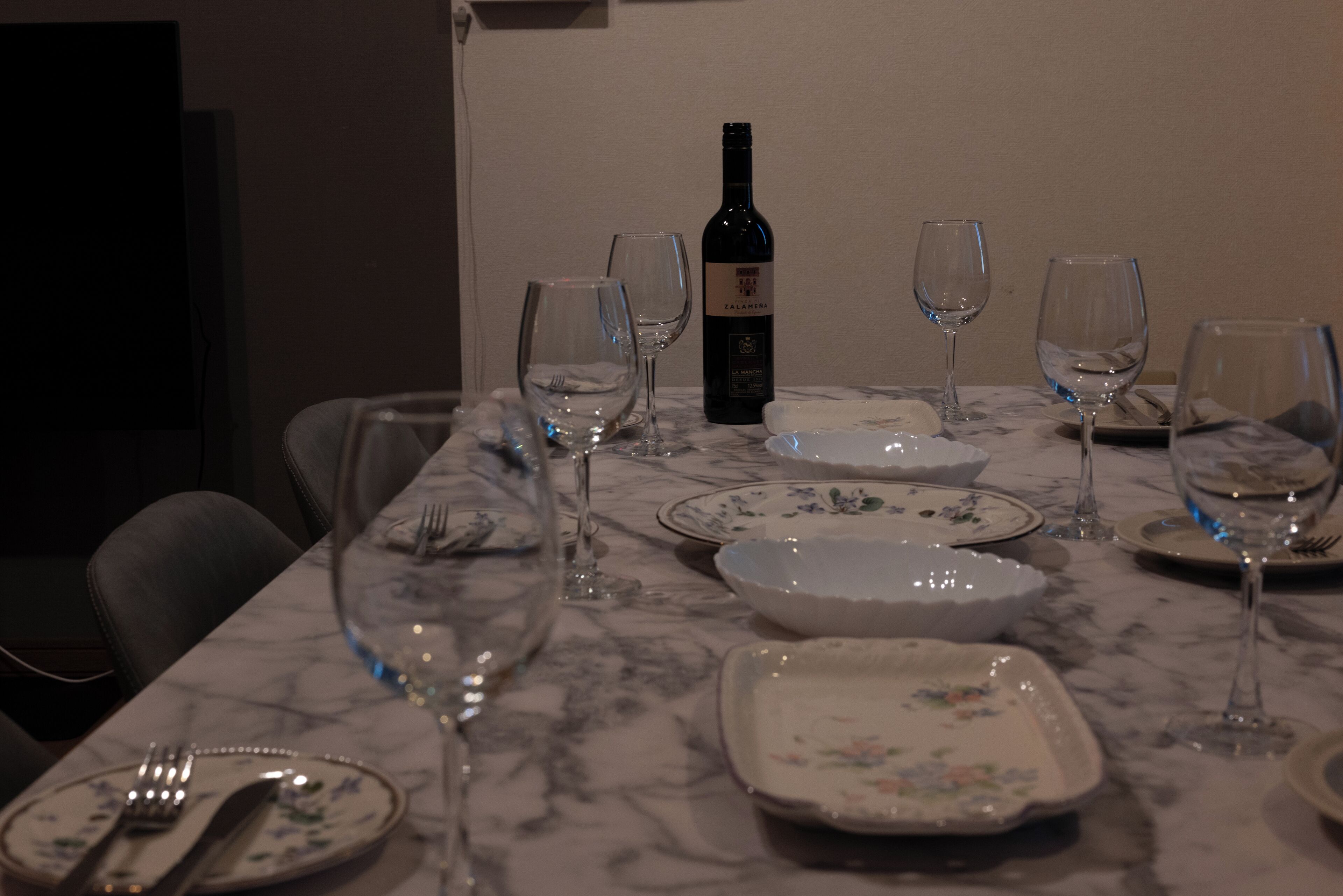 A dining table set with plates, glasses, and a bottle of wine.