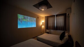 A hotel room with two beds, a wall-mounted projector displaying a nature scene, a standing lamp, and an air conditioning unit. - STAY IN TOKIWA (Asahikawa)
