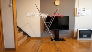 A room with a wooden floor, a TV mounted on the wall, a heater, and a clothes drying rack. - STAY IN TOKIWA (Asahikawa)