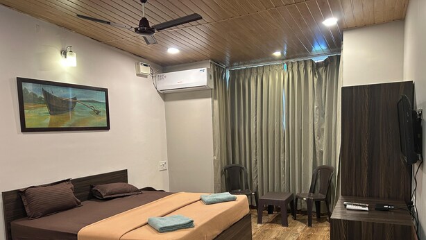 Een slaapkamer met een bed, een bureau, een stoel, een airconditioningapparaat, een plafondventilator en een schilderij aan de muur.