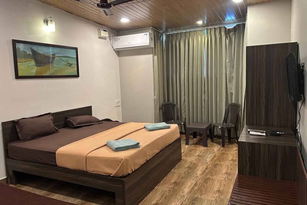 Ein Schlafzimmer mit Bett, Schreibtisch, Stuhl, Klimaanlage, Deckenventilator und einem Bild an der Wand.