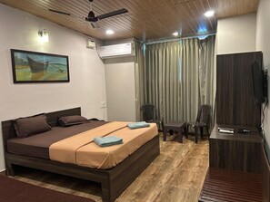 A bedroom with a bed, a desk, a chair, an air conditioning unit, a ceiling fan, and a painting on the wall. - Hotel Coco Homes (Candolim)