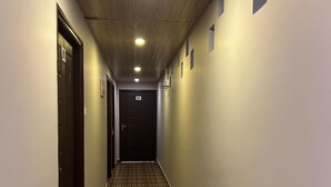 Een gang met houten vloeren, een plafond met inbouwverlichting en deuren aan beide zijden.