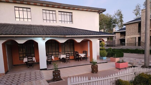 A building with a covered patio area, multiple tables and chairs, and a white picket fence. - Royal Gardens Getaway (Ol Kalou)