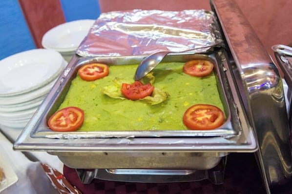 A buffet with a green dish, possibly guacamole, topped with a slice of tomato and lettuce.