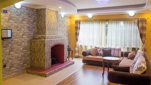 A living room with a stone fireplace, a sofa, and a television mounted on the wall. - Royal Gardens Getaway (Ol Kalou)