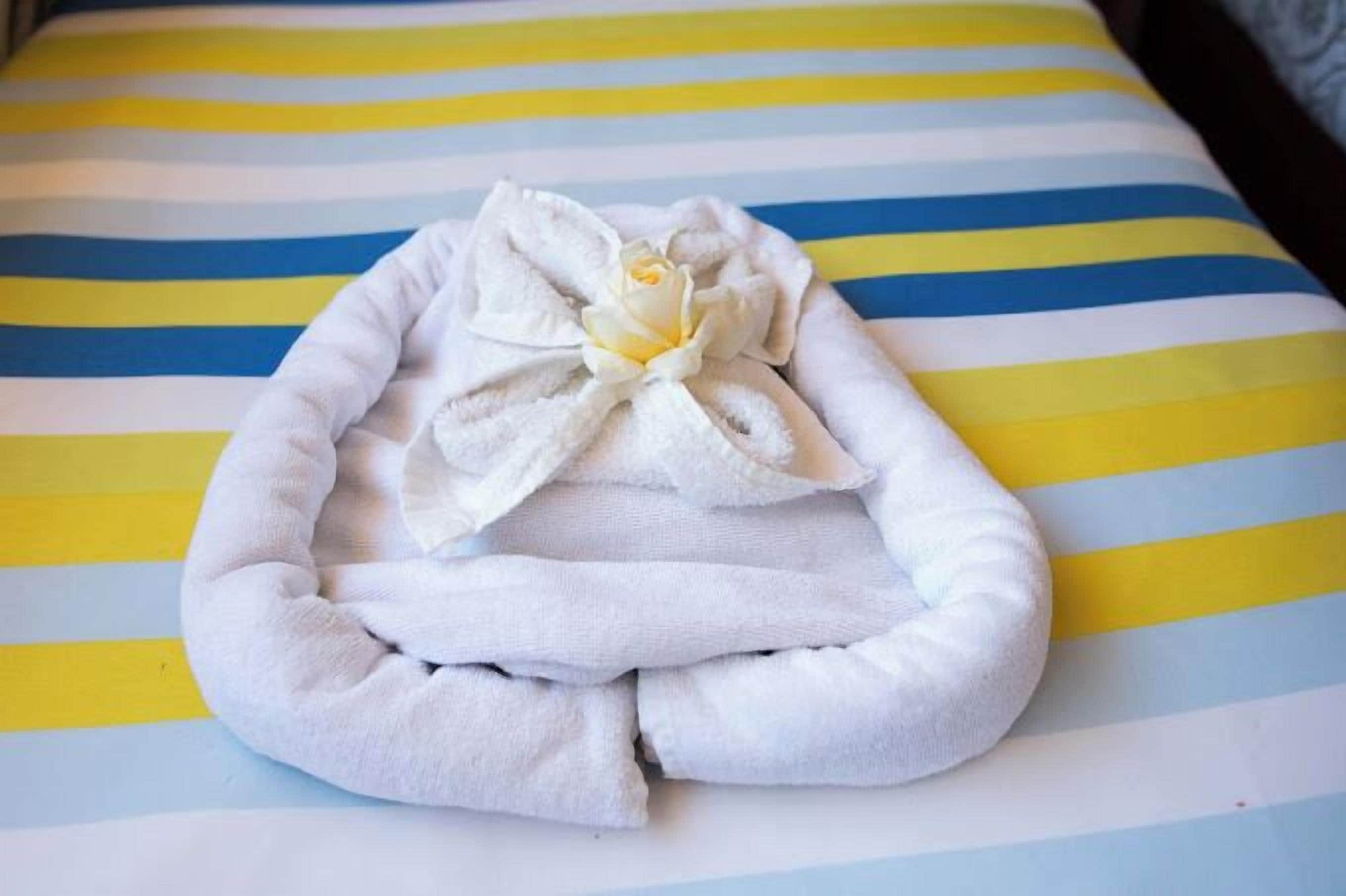 A neatly folded white towel with a flower on a striped bedspread.